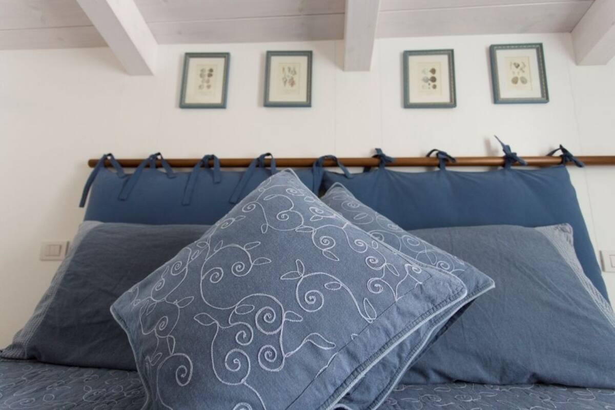 Ein Bett mit blauer Bettwäsche und dekorativen Kissen, ein Holz-Kopfteil und gerahmte Kunstwerke an der Wand.