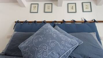 Una cama con ropa de cama azul y almohadas decorativas, cabecera de madera y cuadros en la pared.