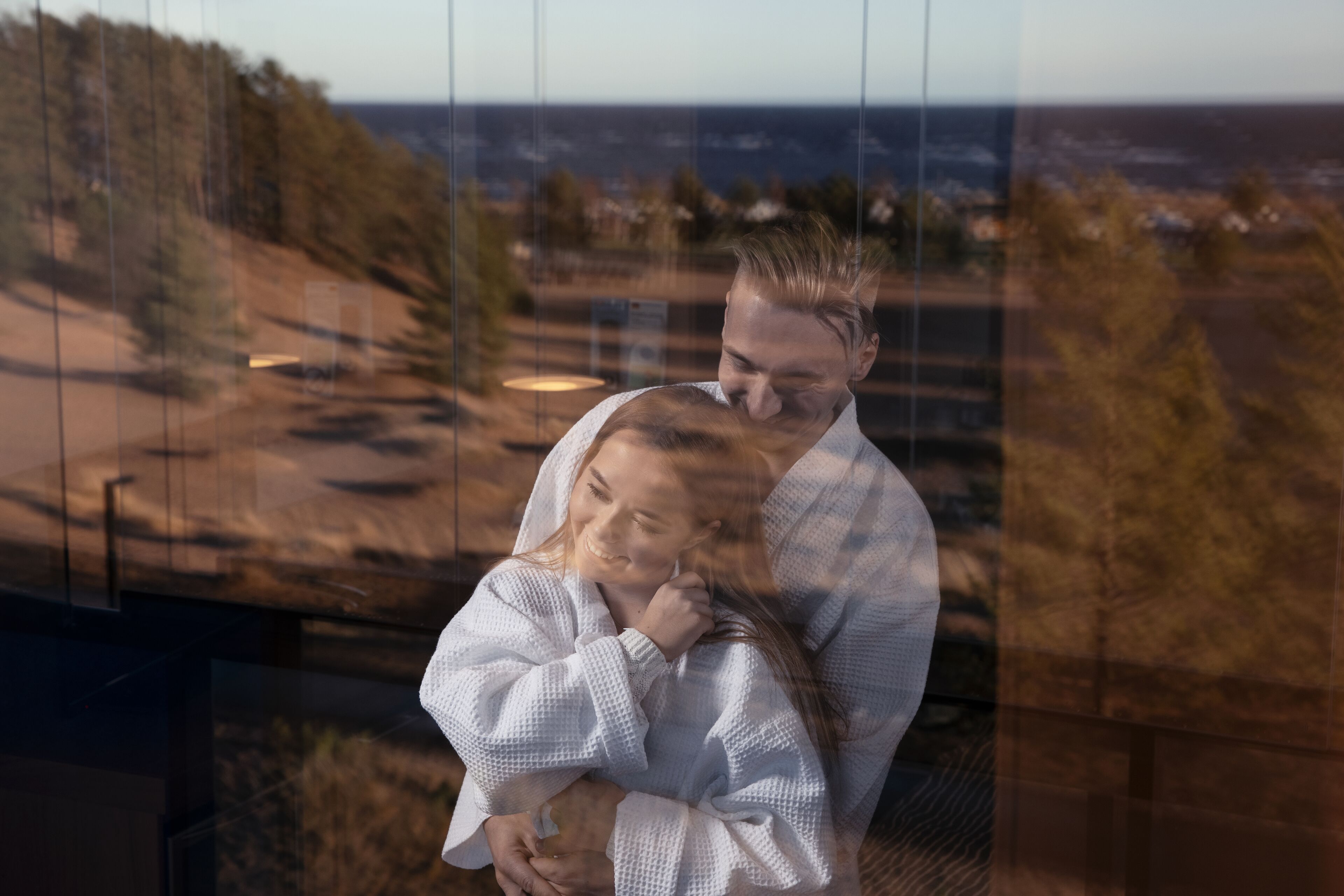 Una pareja abrazándose en una habitación con vistas a un paisaje costero.
