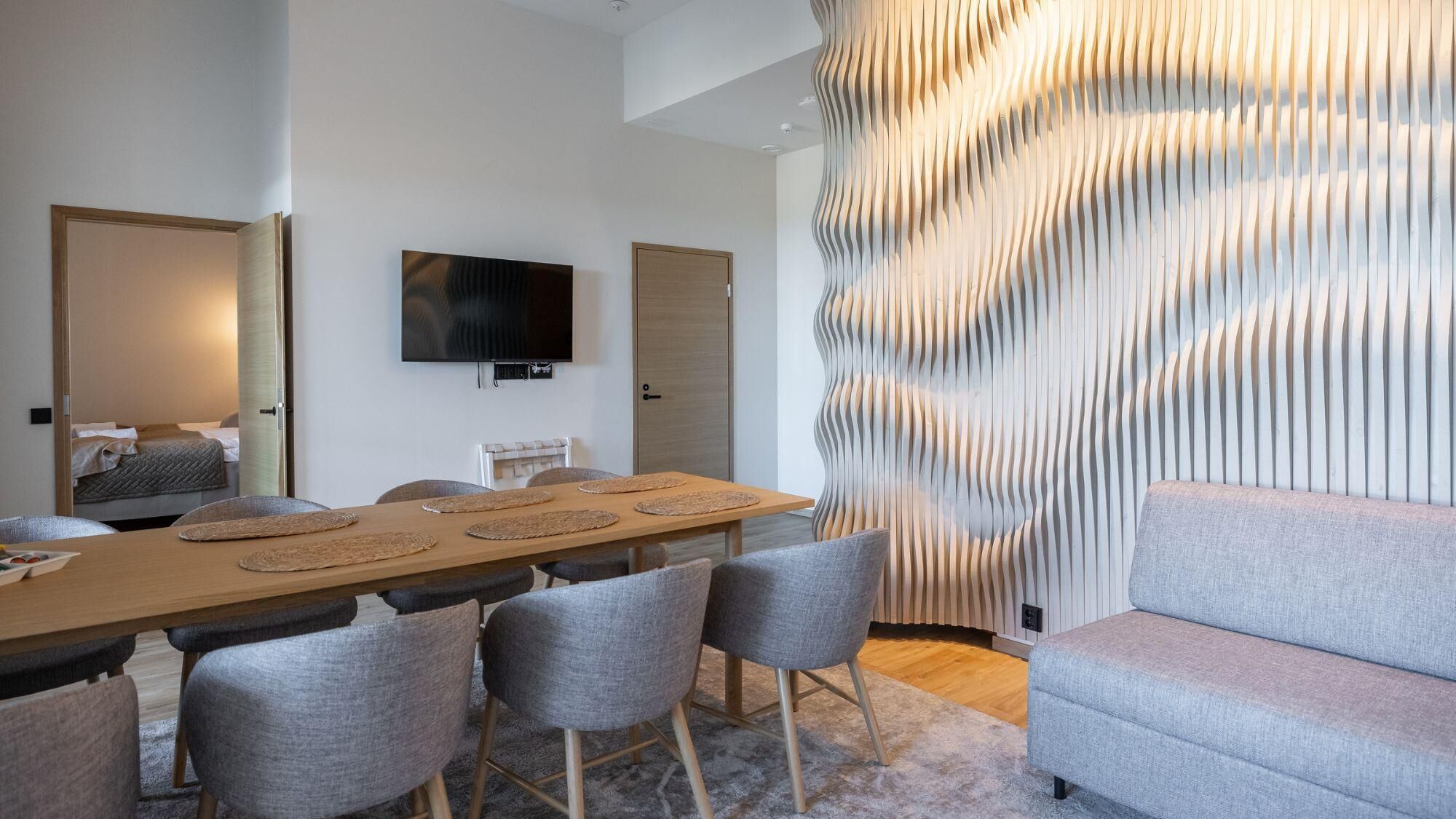 Habitación de hotel moderna con zona de comedor, televisor de pantalla plana y pared con una textura distintiva.