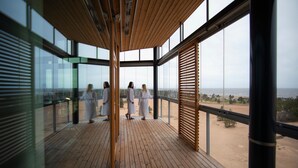 A modern building with large glass windows, a wooden deck, and a view of the beach.