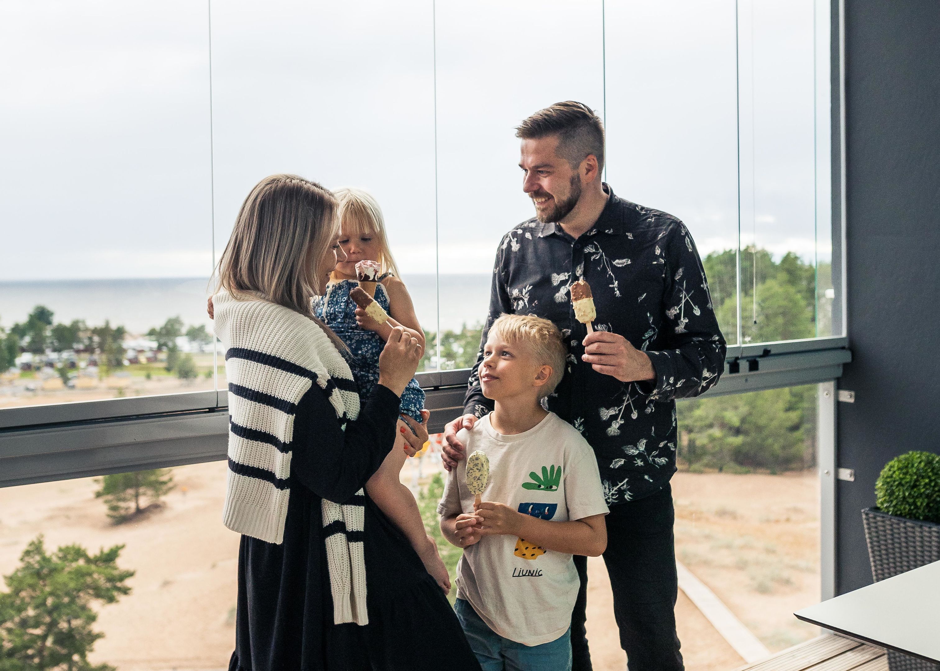 Eine Familie genießt Eis auf einem Balkon mit Blick aufs Meer.