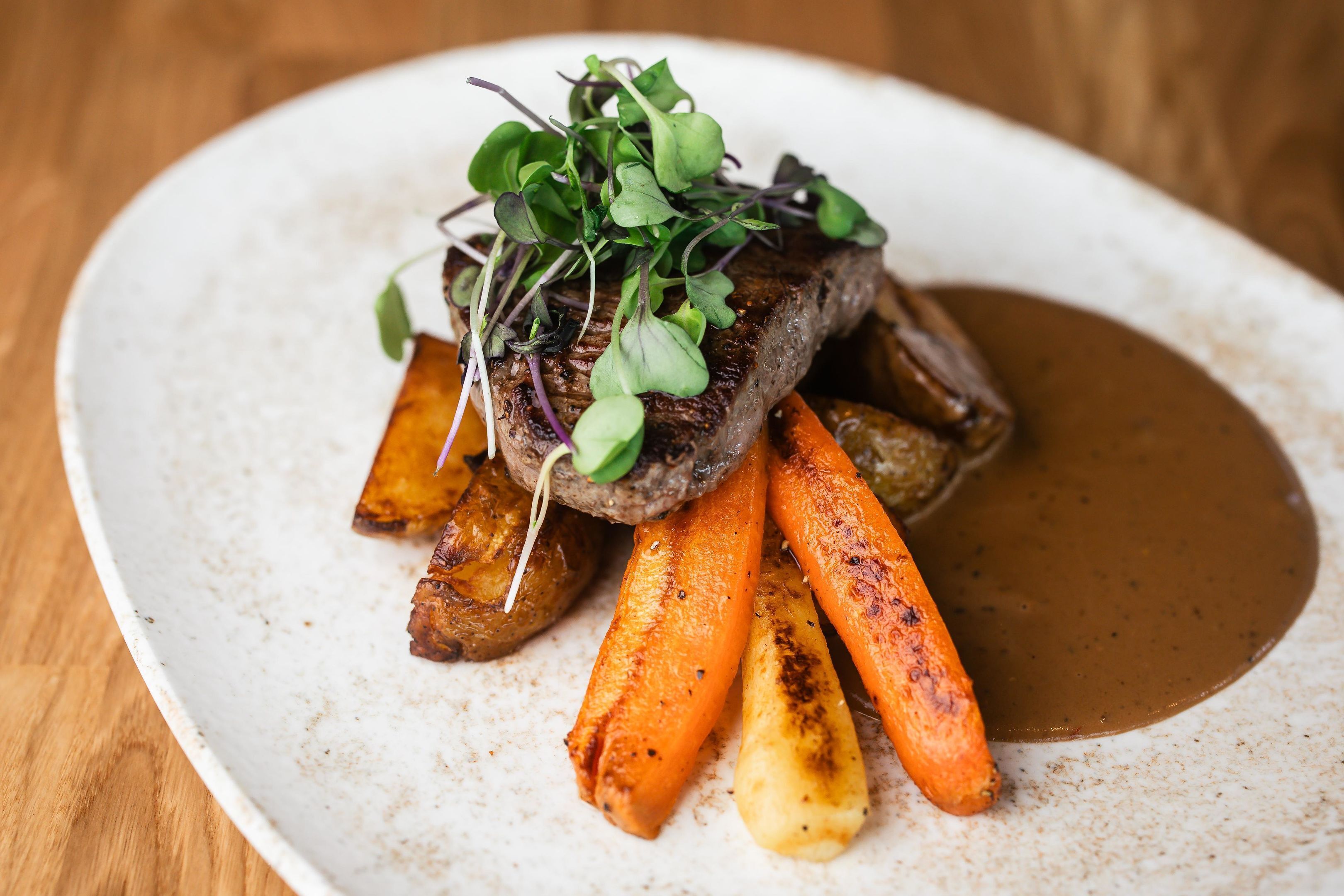 A plate with a steak, carrots, and a sauce.