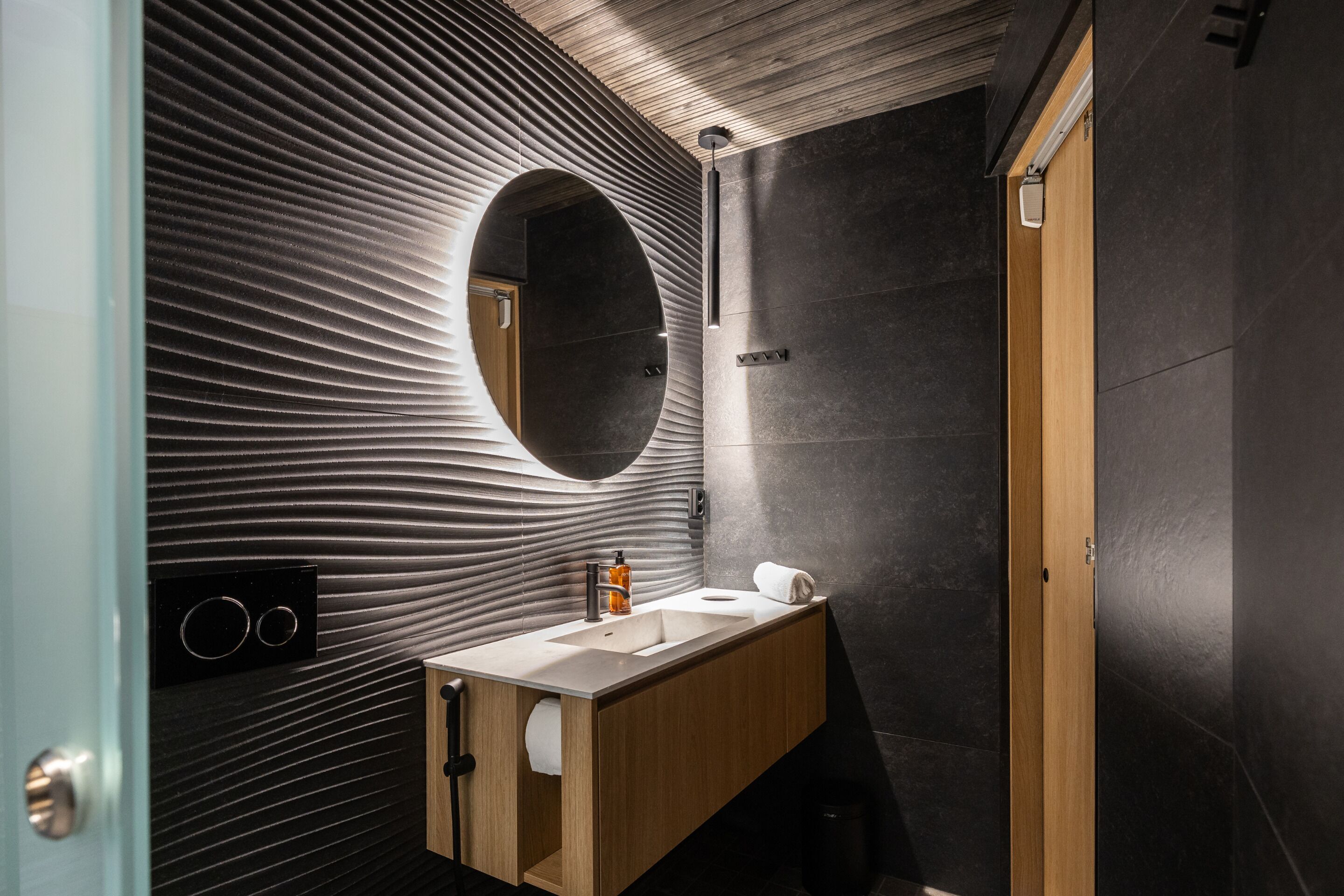 Un baño moderno con un tocador de madera, un espejo grande y una pared con textura.