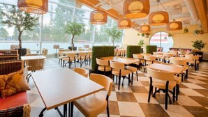 A spacious indoor dining area with multiple tables and chairs, large windows, and hanging wicker lamps.