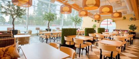 A spacious indoor dining area with multiple tables and chairs, large windows, and hanging wicker lamps.