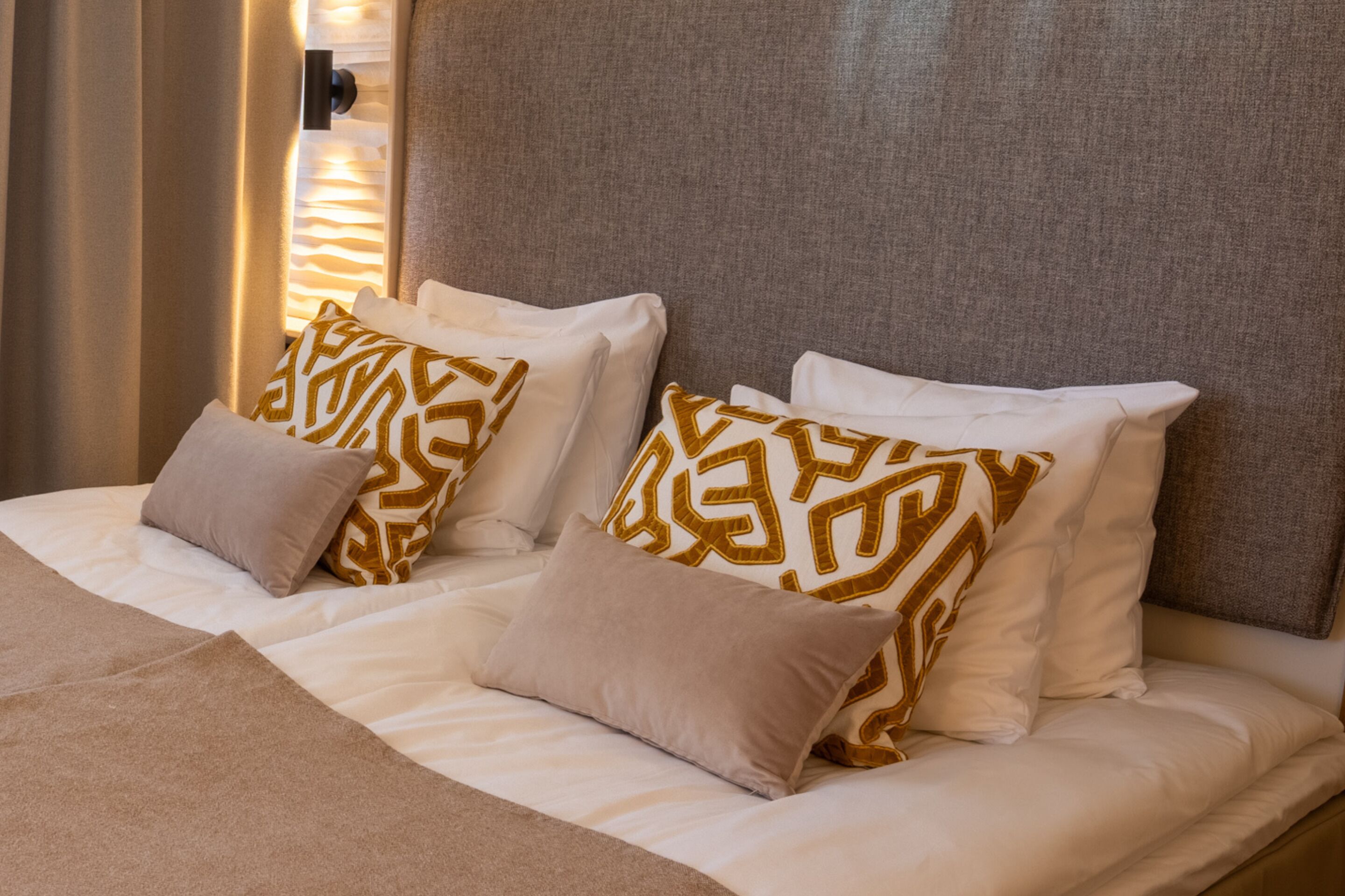 A neatly made bed with white and beige bedding, two patterned pillows, and a headboard.