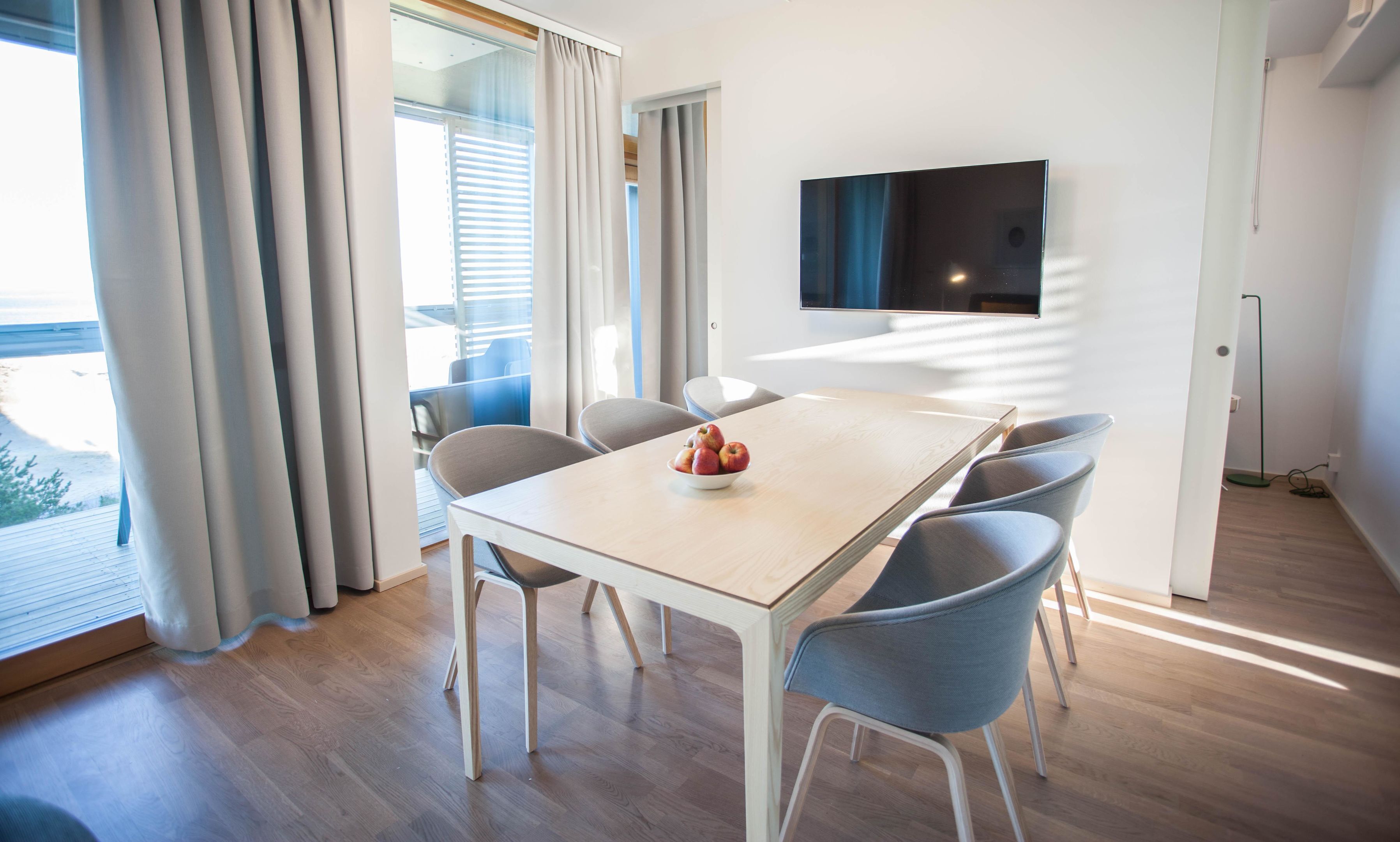 A modern dining area with a wooden table, grey chairs, and a bowl of fruit.