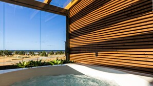 A hot tub with a view of the ocean, wooden slats on the wall, and green plants.