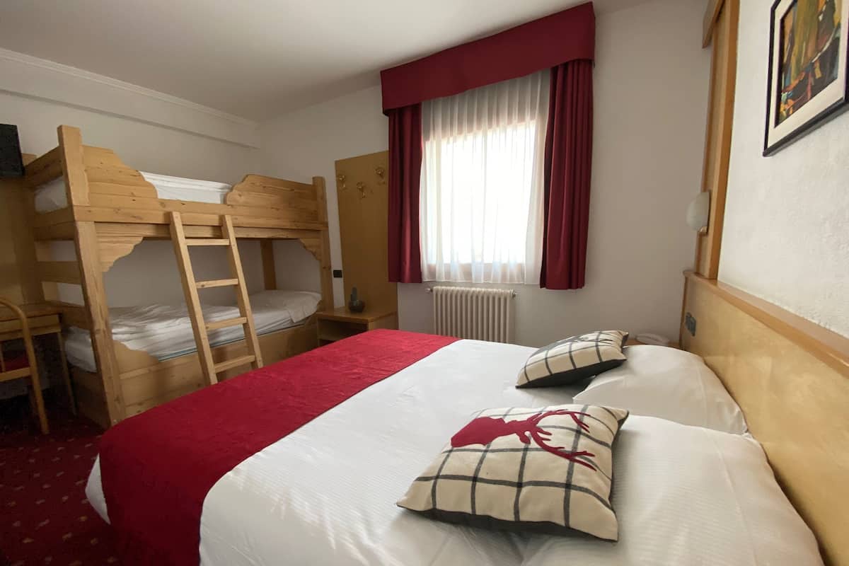 Una habitación con una litera, una cama individual con una manta roja y una ventana con cortinas rojas.