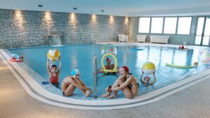 En inomhuspool med väggar av sten, en konstgjord vattenfallskaskad och ett stort antal uppblåsbara leksaker.