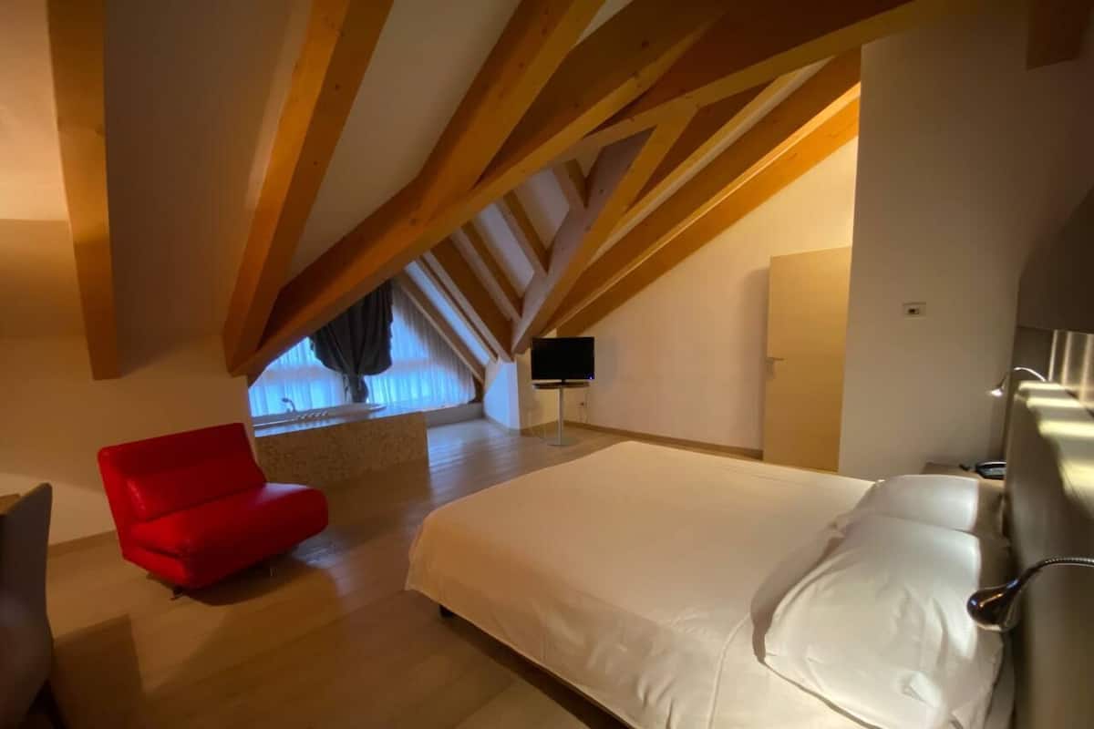 Un dormitorio con una cama grande, una silla roja y un tragaluz.