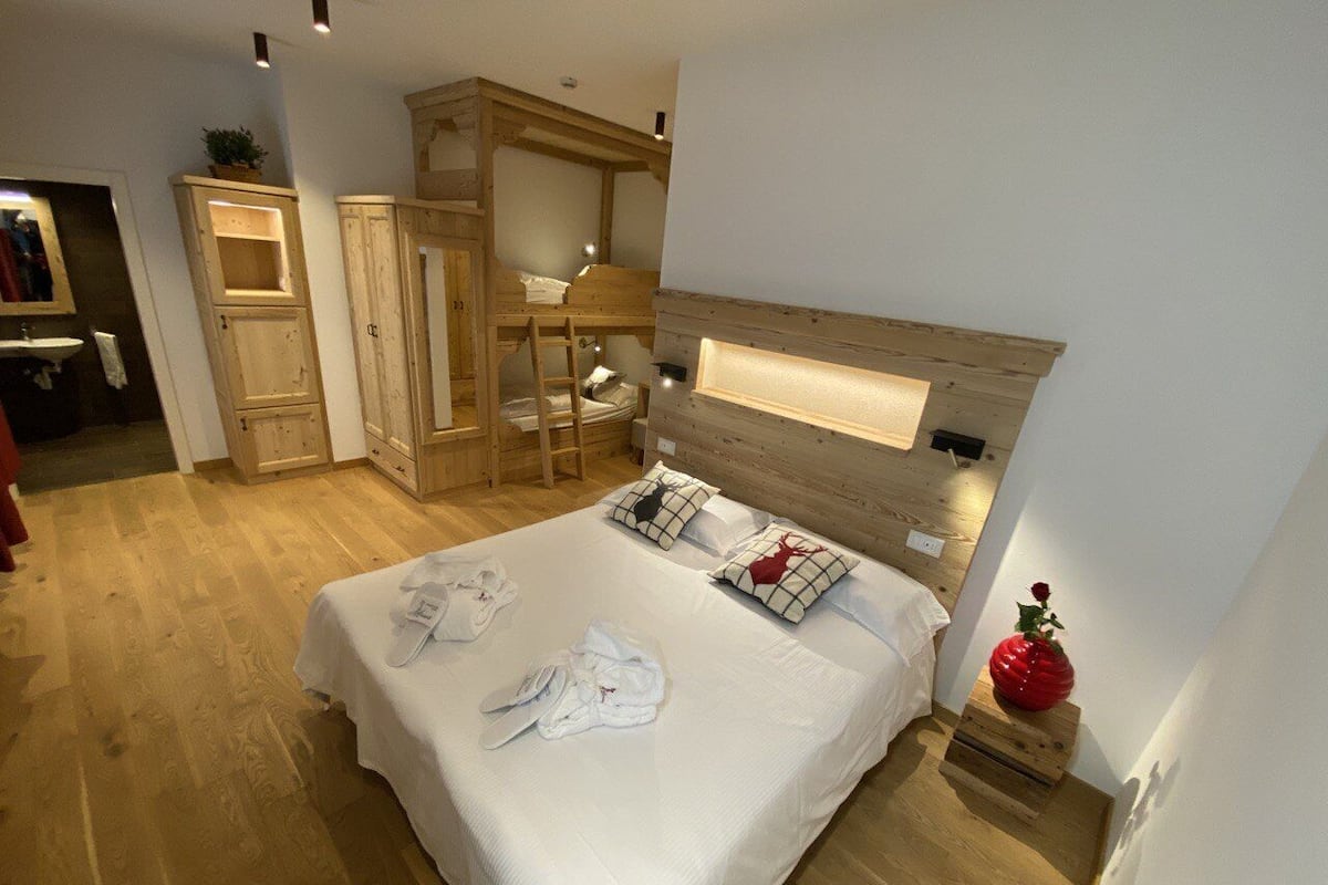 Un dormitorio con una cama litera de madera, una mesita de noche con lámpara y un jarrón decorativo rojo.