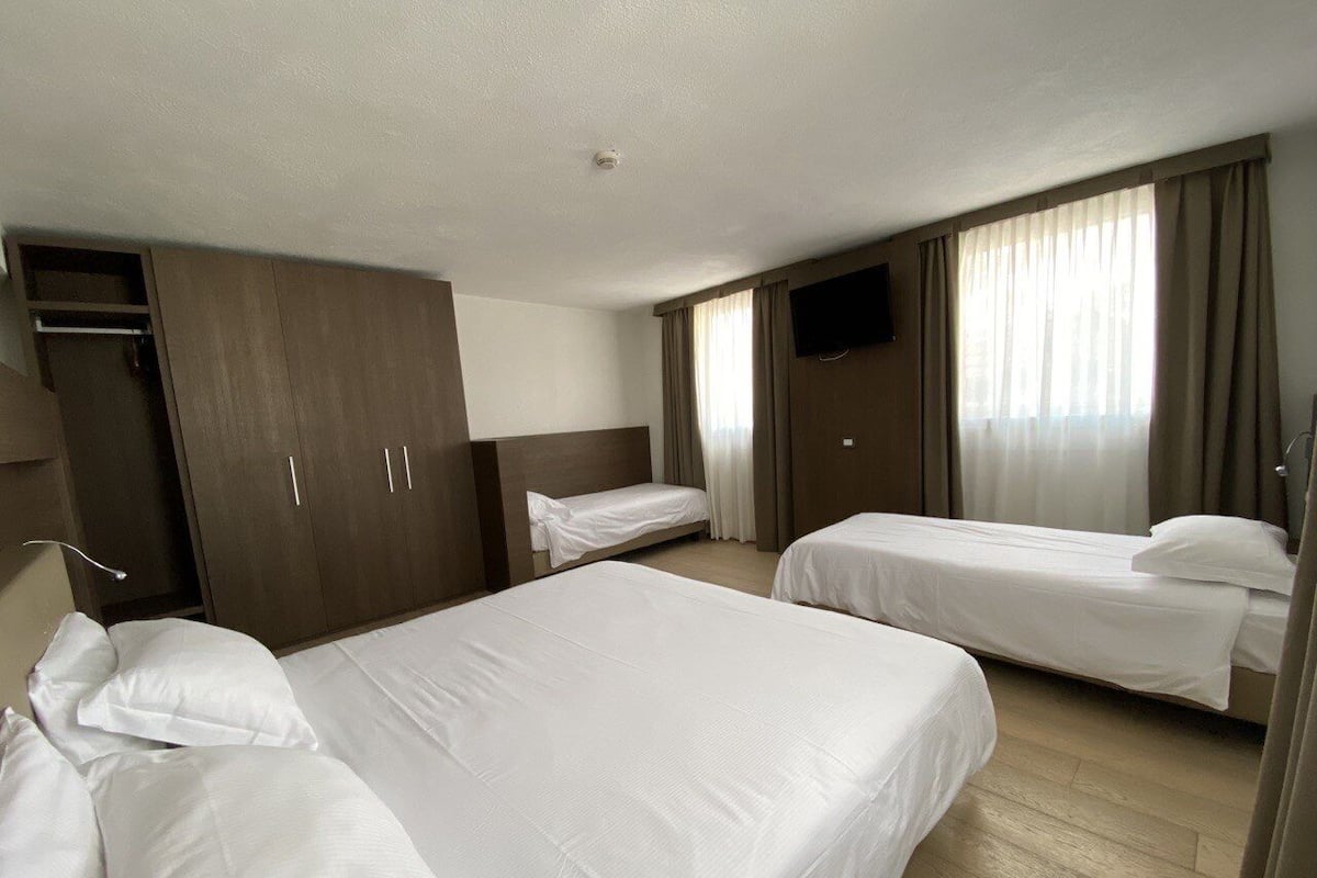 Habitación de hotel con dos camas, un armario, televisor y ventana con cortinas.