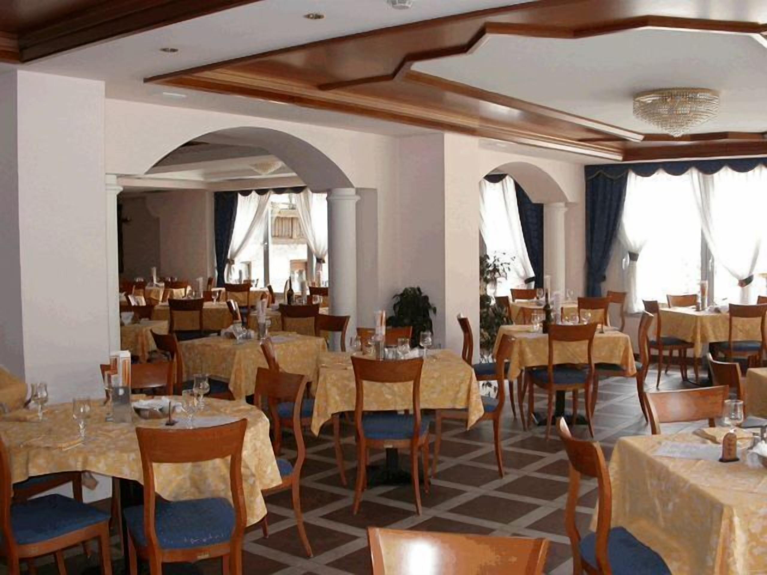 Ein Restaurant mit mehreren Tischen und Stühlen, ansprechend angeordnet in einem großzügigen Raum mit hohen Decken und dekorativen Verzierungen.
