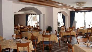 Ein Restaurant mit mehreren Tischen und Stühlen, ansprechend angeordnet in einem großzügigen Raum mit hohen Decken und dekorativen Verzierungen.