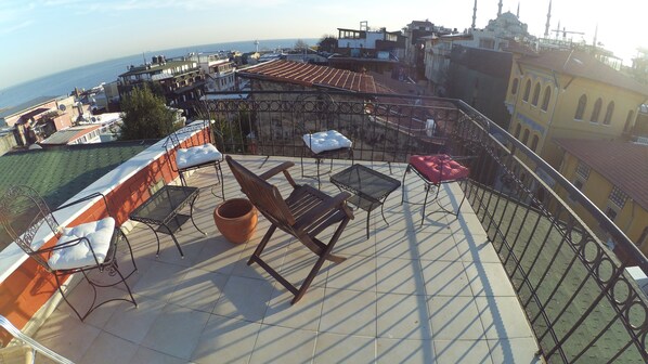 Terraço no telhado com mobiliário ao ar livre, vista da cidade e um corpo de água distante.