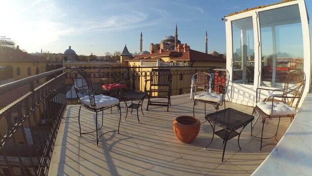 Terraço no telhado com área de estar externa, uma janela grande e vista para uma mesquita com minaretes.