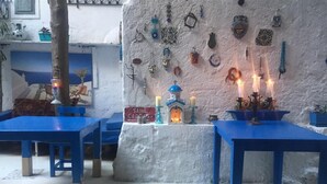 Um quarto com mesas e cadeiras azuis, um pequeno santuário com velas e objetos decorativos nas paredes.