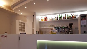 A hotel reception area with a counter, shelves of liquor bottles, a coffee machine, and a sign for Orzo Espresso. - Hotel Mizar (Rimini)