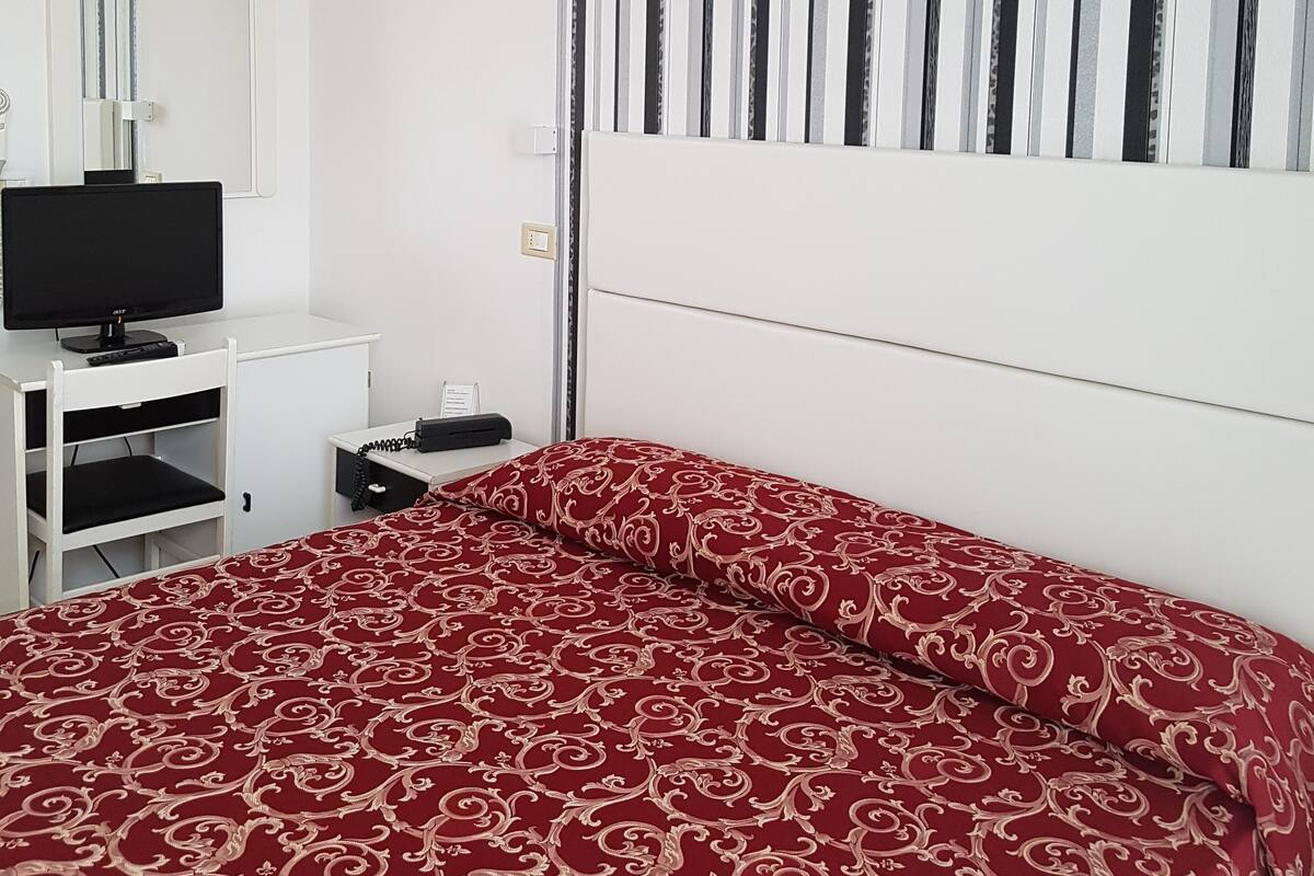 A bedroom with a bed, a TV, a desk, and a striped curtain.
