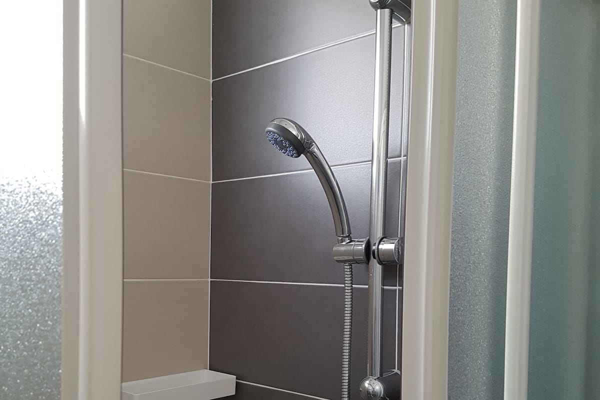 A shower enclosure with a handheld showerhead and a wall-mounted faucet.