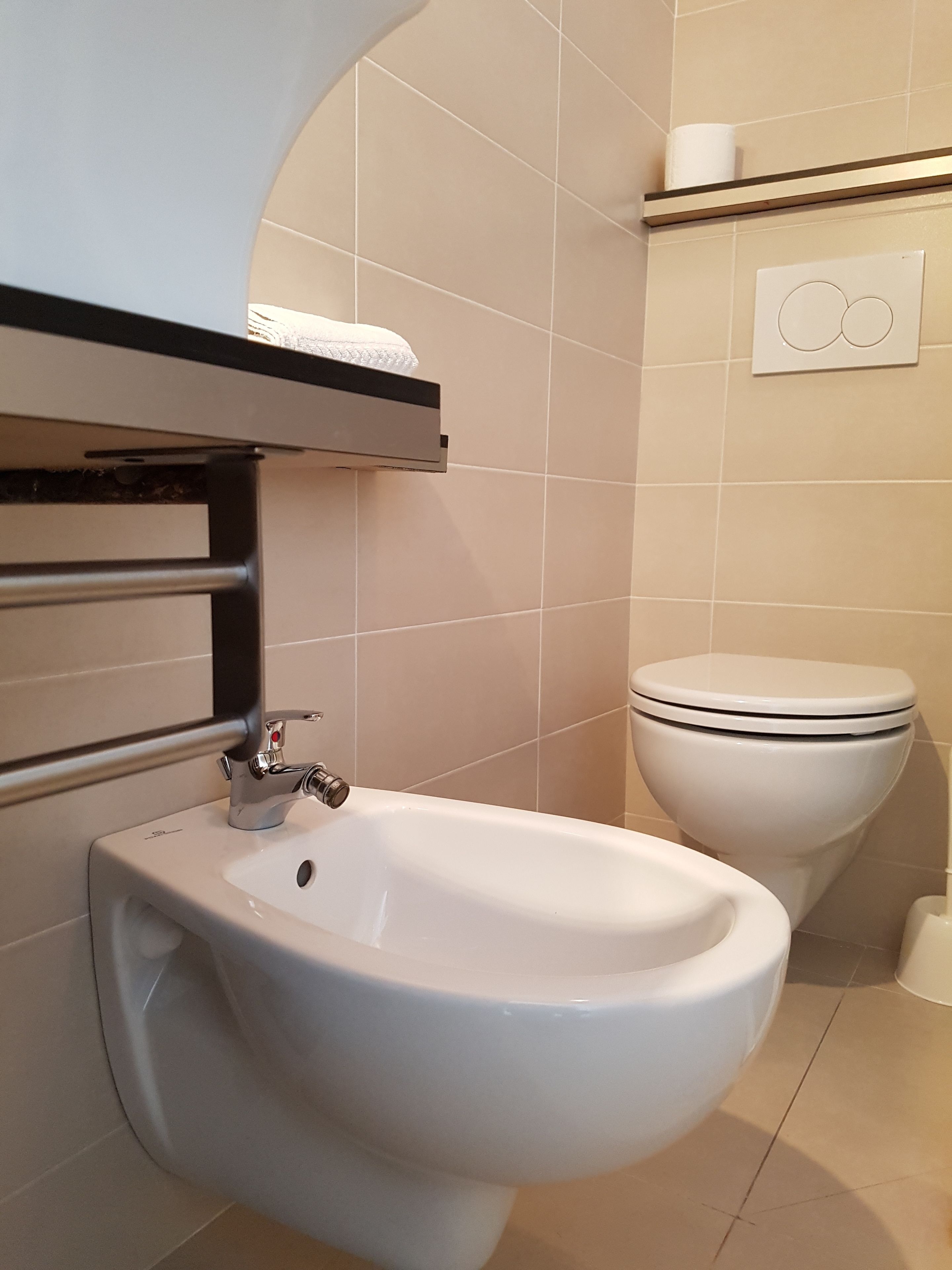 A bathroom with a bidet, a toilet, and a towel rack.