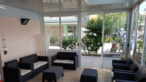 A modern indoor seating area with wicker furniture and a glass door leading outside. - Hotel Mizar (Rimini)