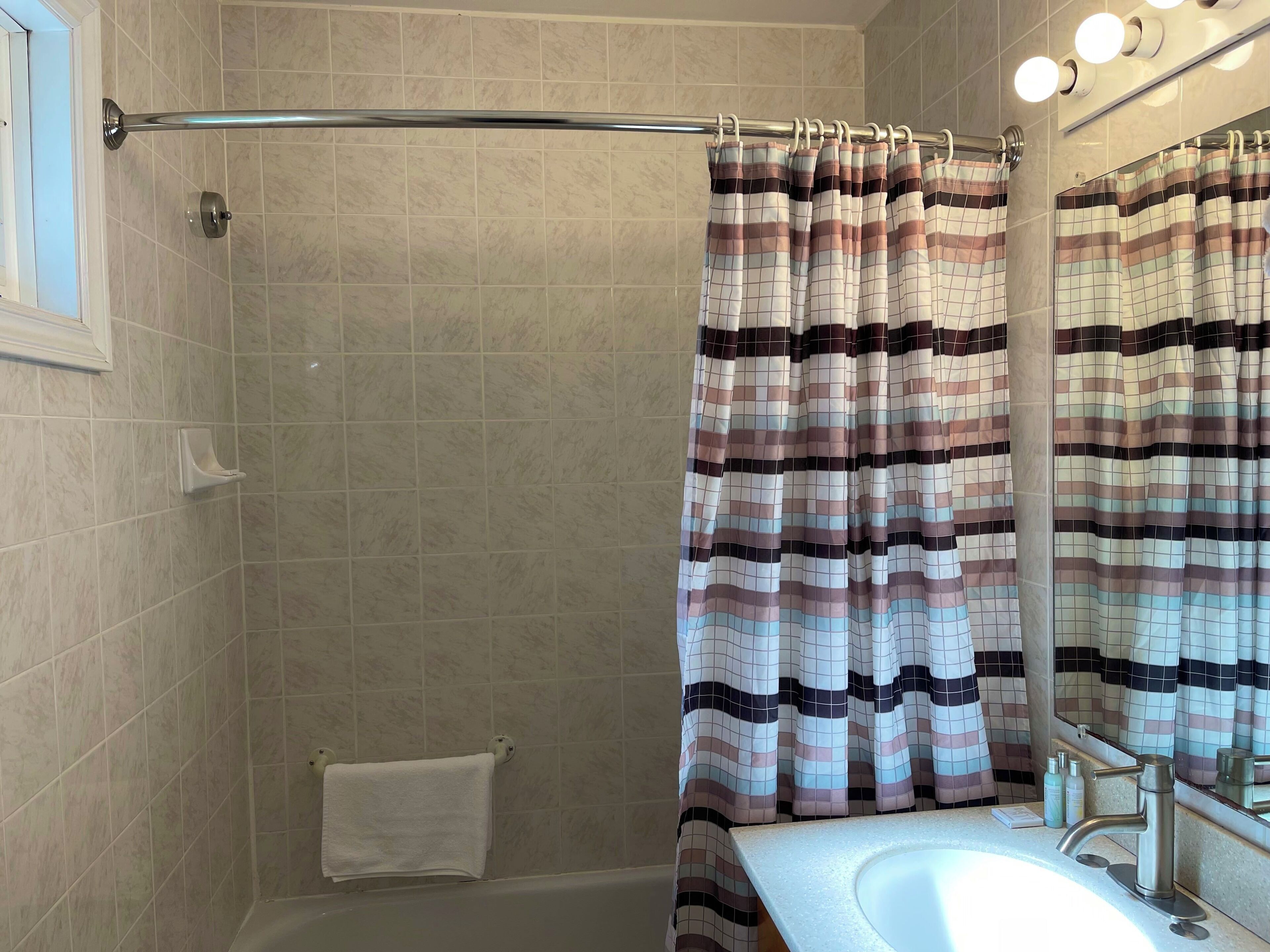 A bathroom with a shower curtain, a bathtub, a sink, and a mirror.