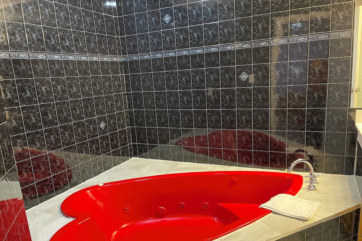 Un baño con una bañera roja, baldosas de mármol oscuro y una toalla blanca sobre el mostrador.