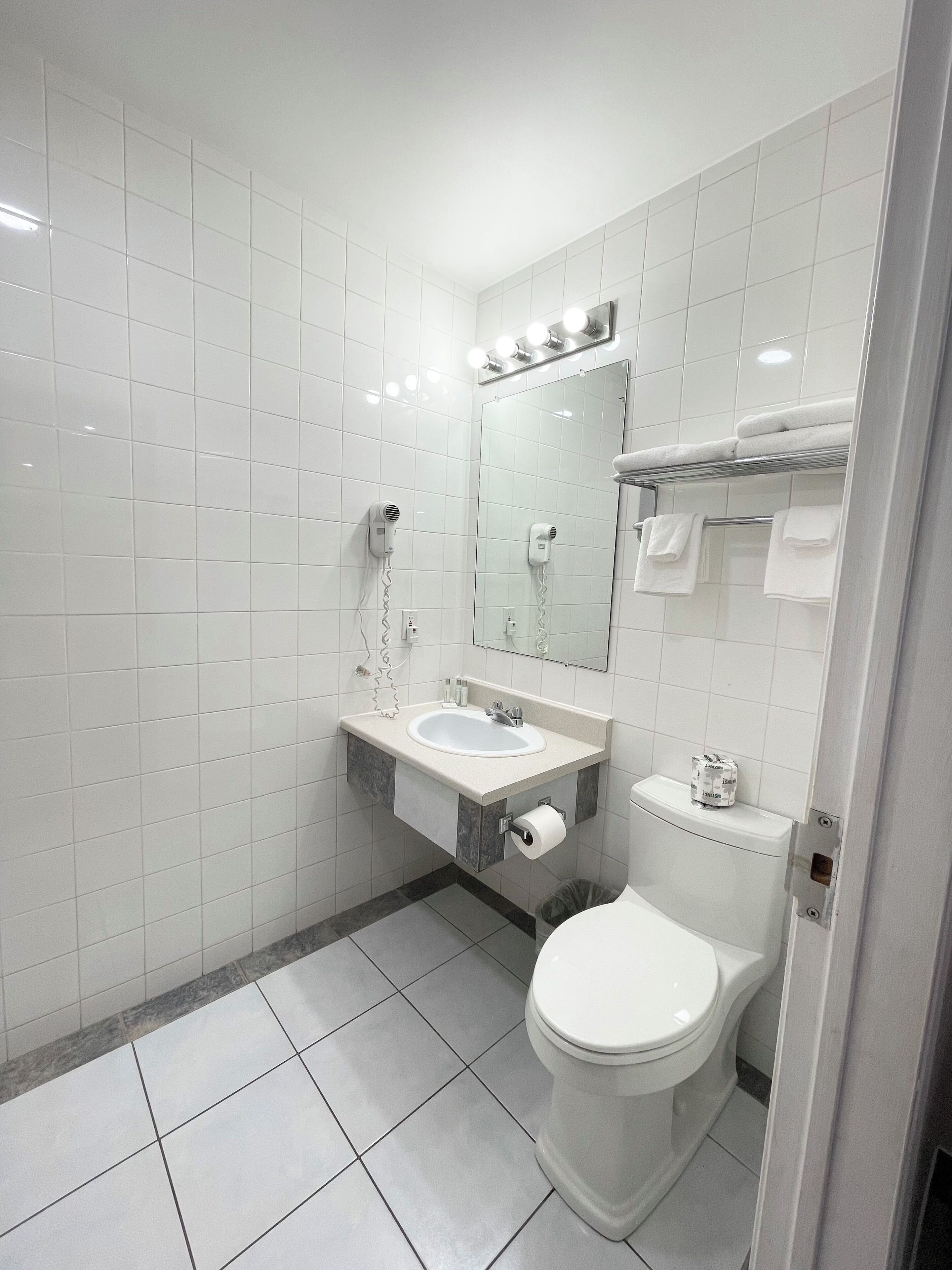 Une salle de bain moderne avec des carreaux blancs, un lavabo, un miroir avec éclairage intégré, un porte-serviettes et des toilettes.