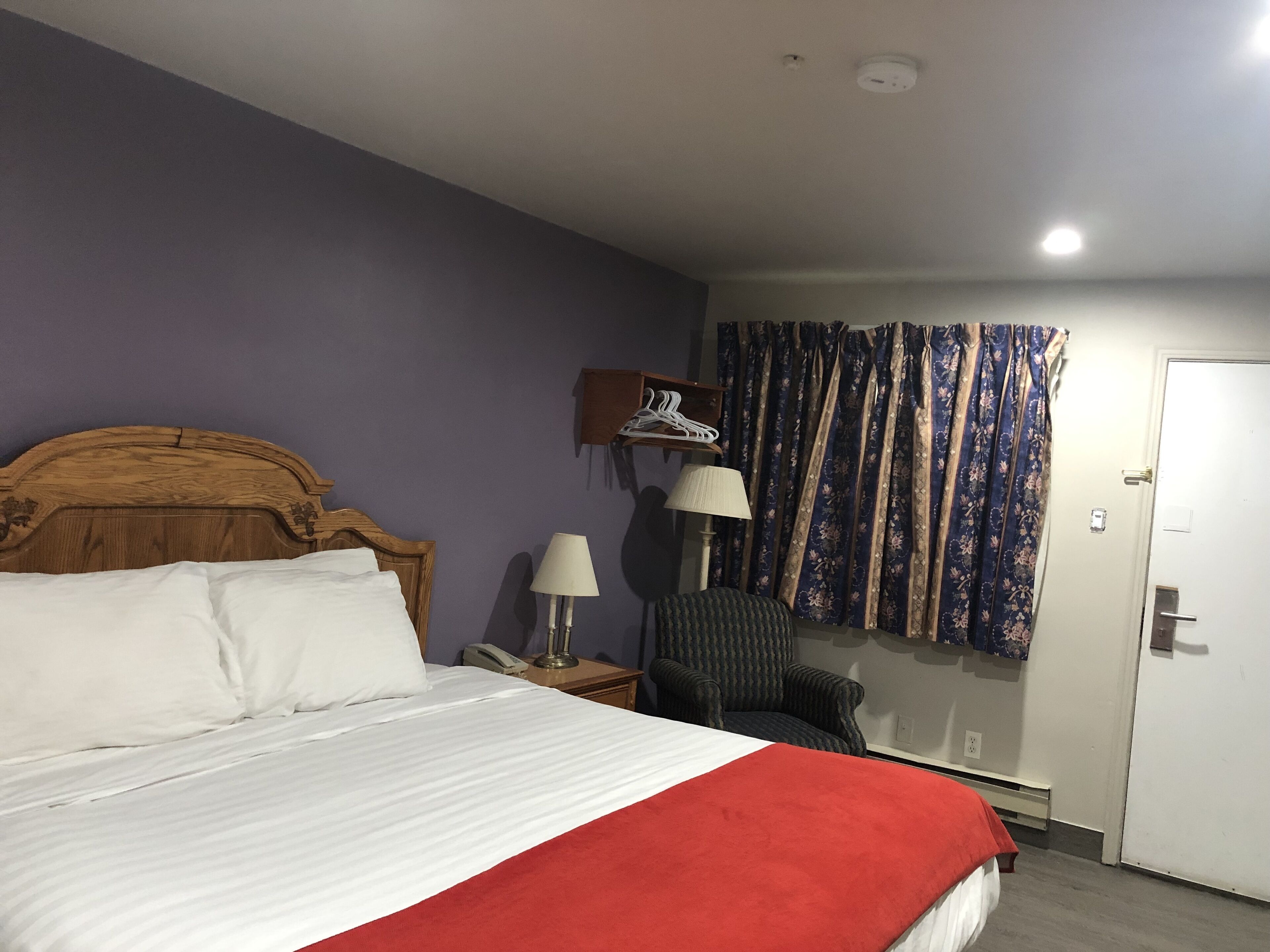 A hotel room with a bed, a chair, a lamp, a phone, and a door.