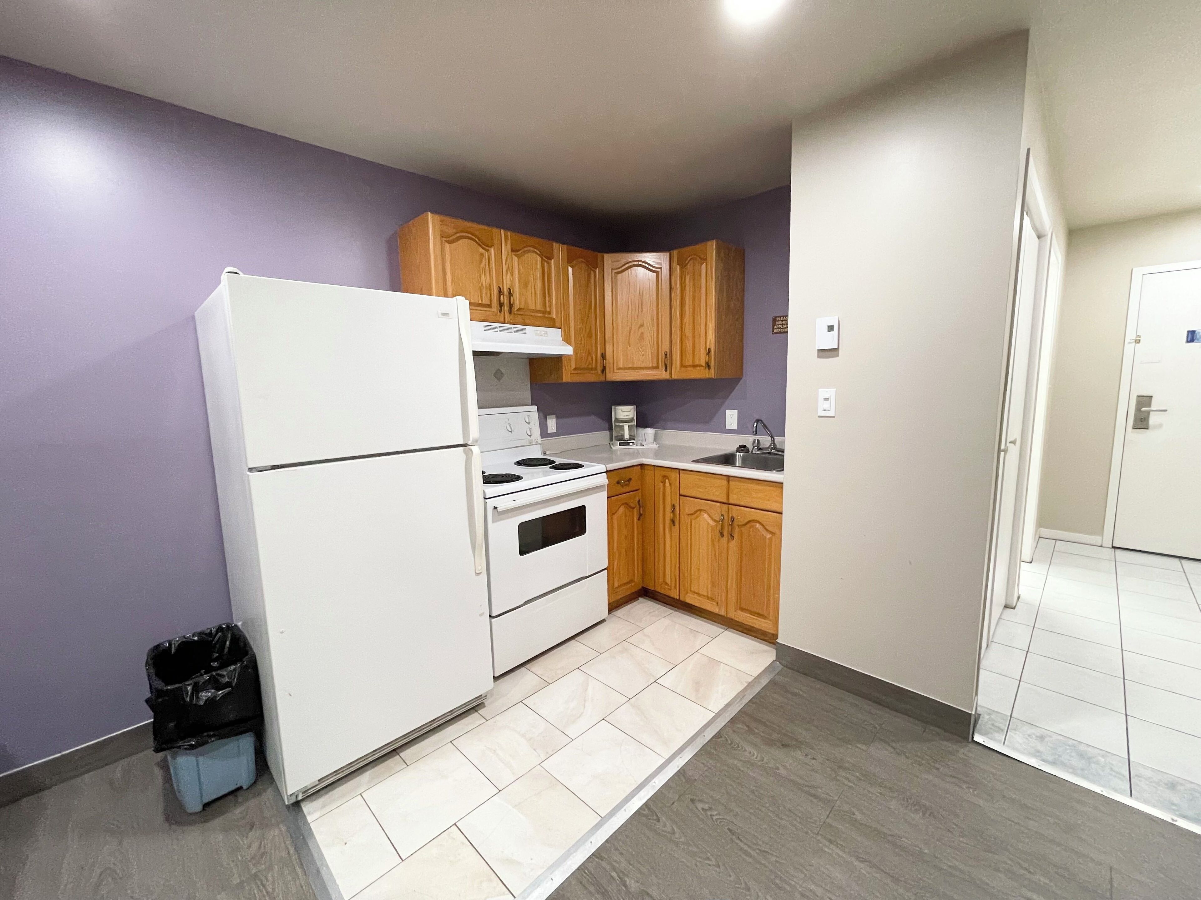 A compact kitchen with a refrigerator, stove, and wooden cabinets.