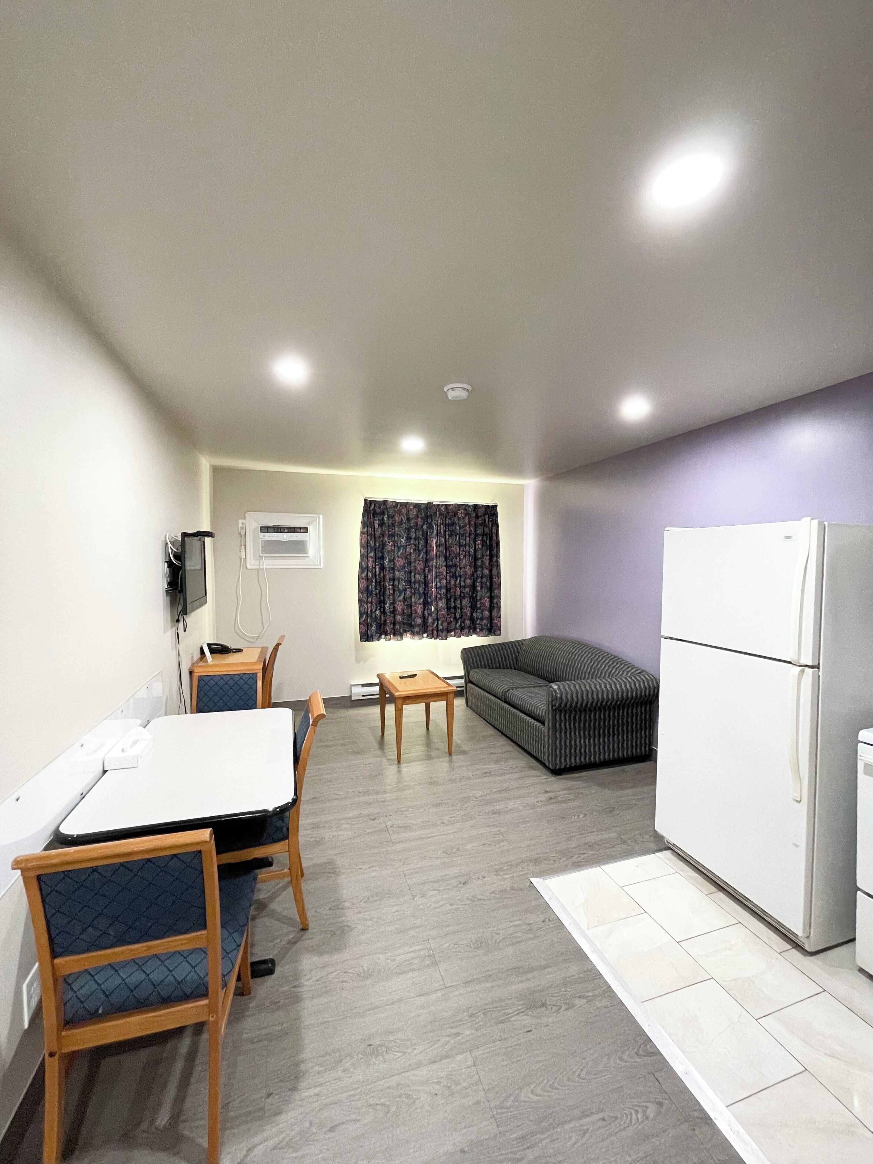 A compact living space with a dining table, chairs, a sofa, a refrigerator, and a window with curtains.