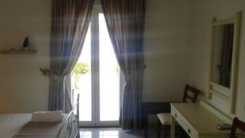 A room with a bed, a desk, a chair, and a mirror. There is a window with curtains and a view outside.