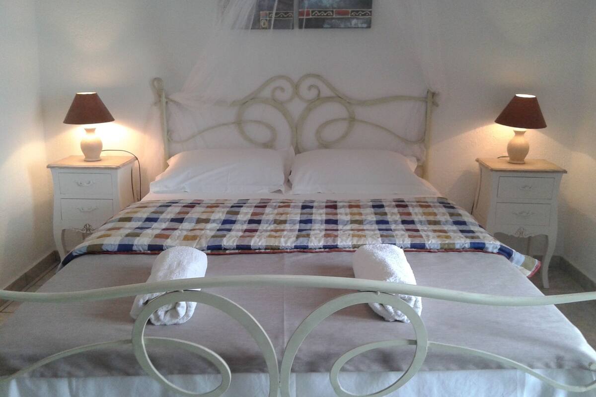 A neatly made bed with a checkered blanket, two bedside lamps, and two white towels on the bed.