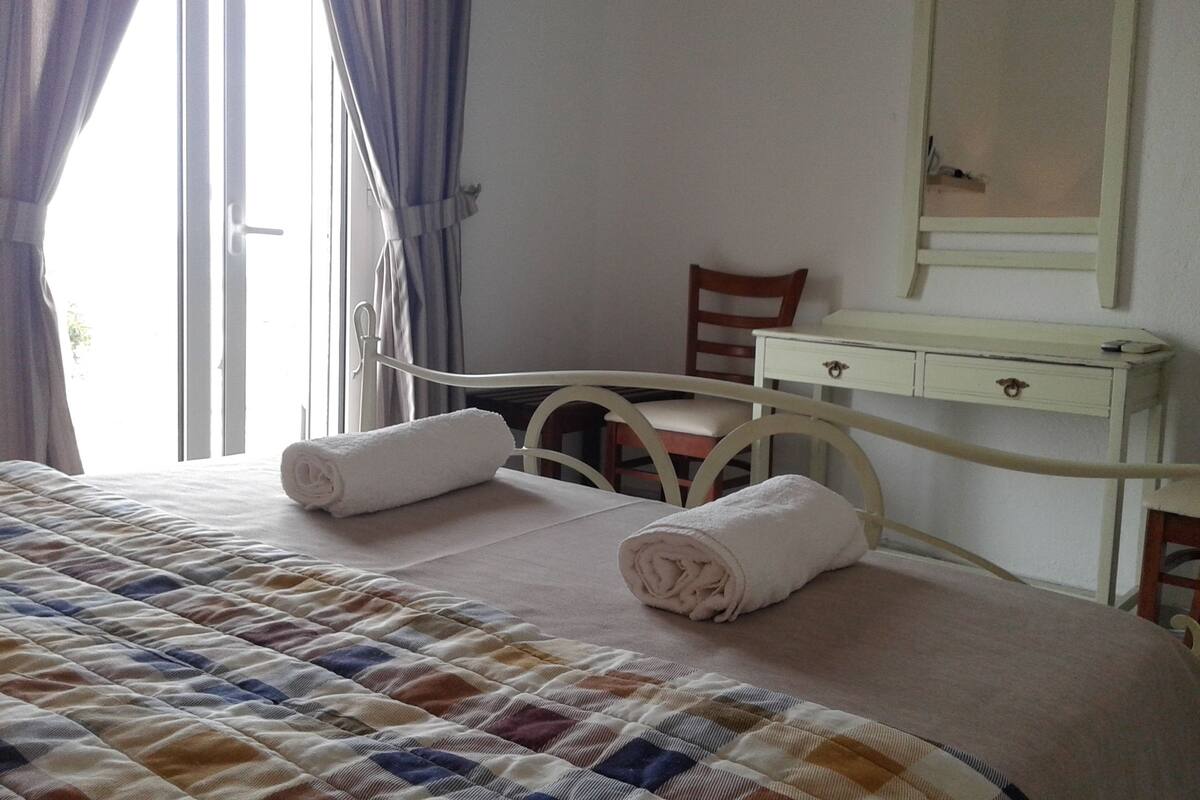 A hotel room with a bed, a bedside table, a chair, and a mirror.