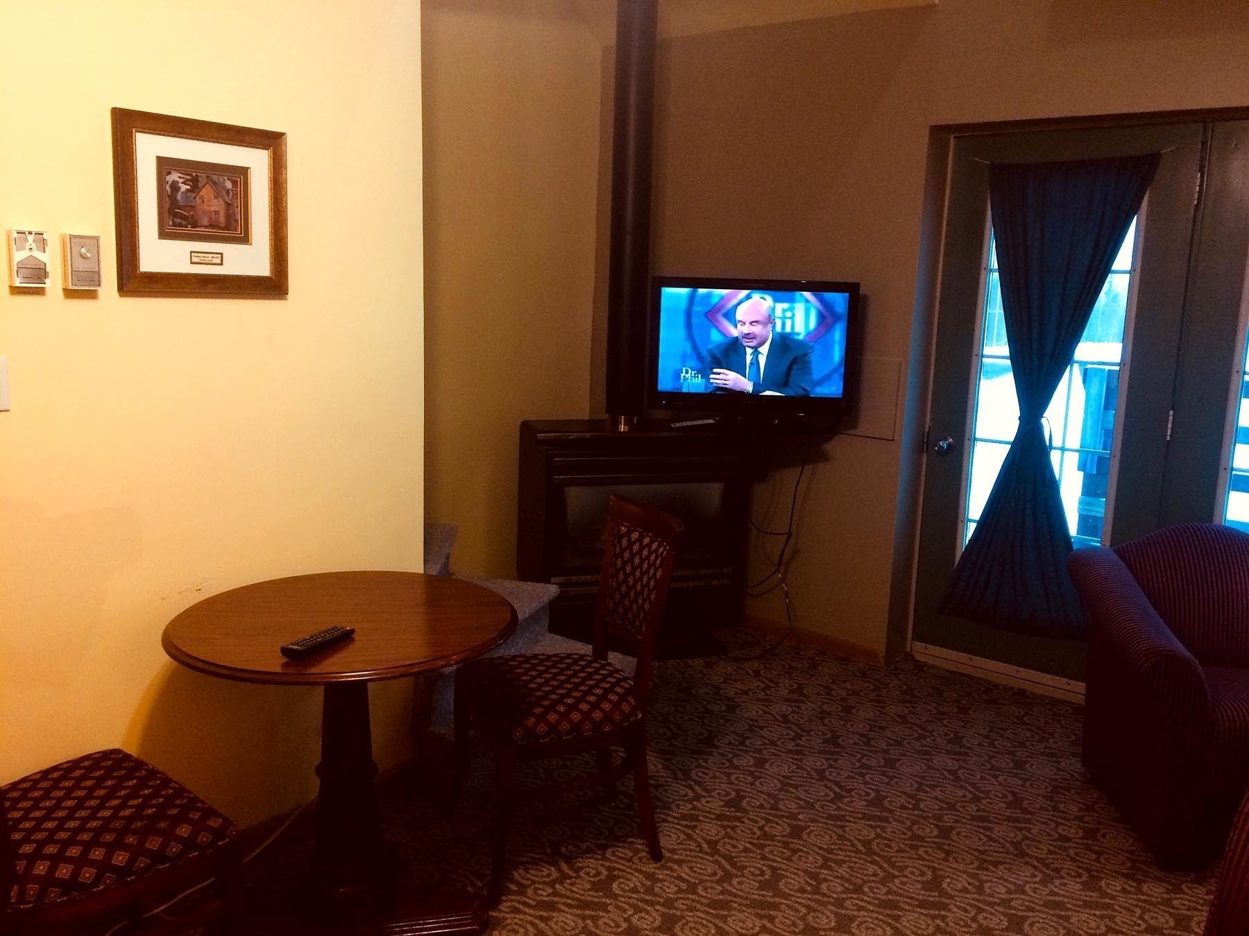 A hotel room with a television, a small table, a chair, and a patterned carpet.