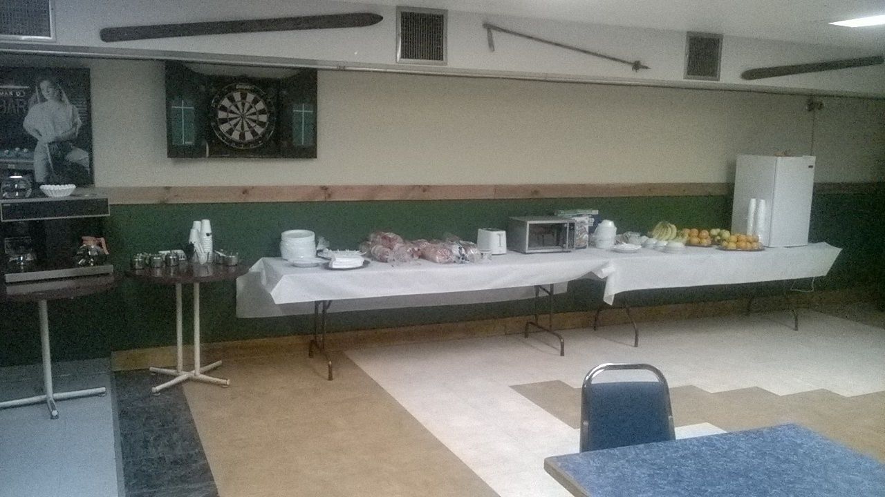 Una habitación con una larga mesa dispuesta para una comida, un dardo y un refrigerador.