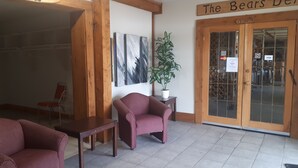 A reception area with wooden beams, a red upholstered chair, a small table, and a potted plant. There are two framed abstract paintings on the wall and a sign above the door that reads "The Bears Den." - North Adventure Inn (Cochrane)