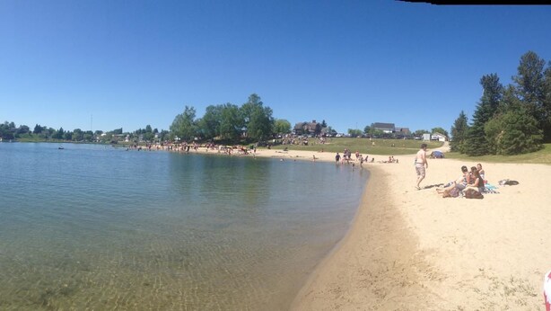 A lake with a sandy beach, surrounded by trees and buildings in the background. - North Adventure Inn (Cochrane)