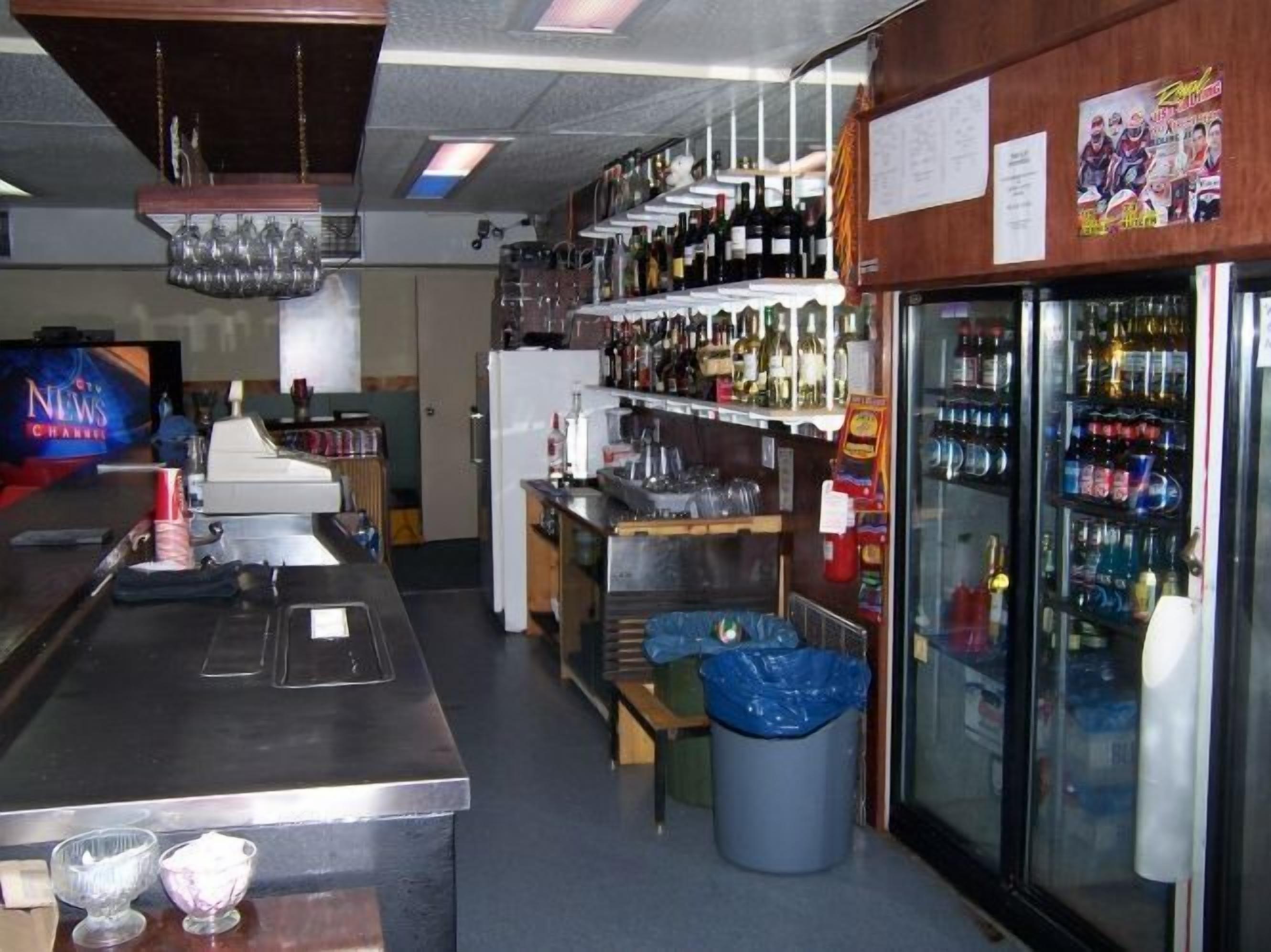 Eine Bar mit Regalen voller Flaschen, einem Kühlschrank und einem Mülleimer.