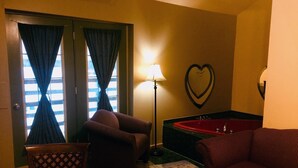 A hotel room with a red bathtub, two striped armchairs, a wooden chair, and a heart-shaped wall decoration. - North Adventure Inn (Cochrane)
