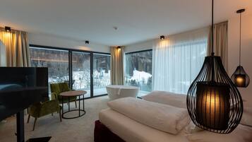 Habitació d'hotel moderna amb un llit gran, televisió, zona de seients i vista a un paisatge nevà a través de les finestres.