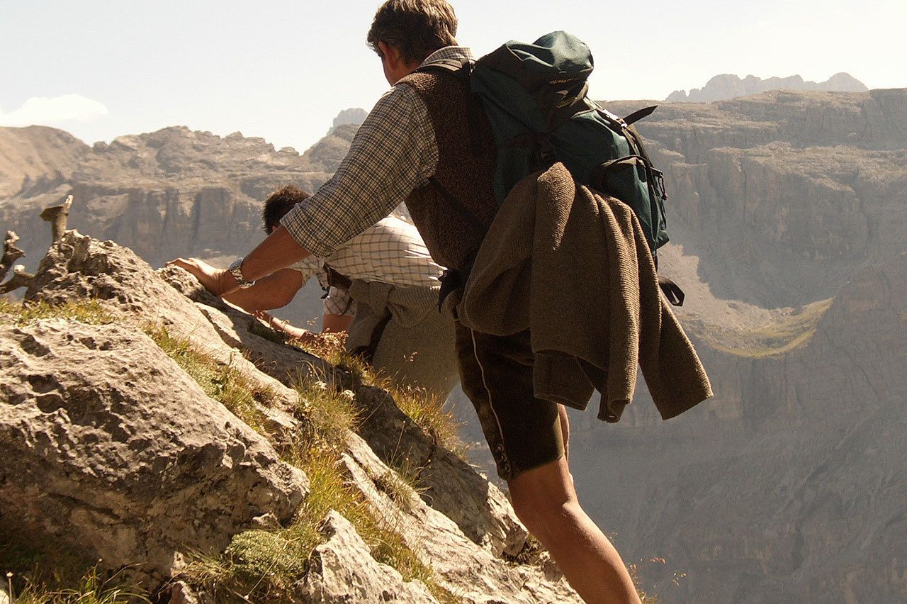 A person hiking on a rocky mountain path with a backpack and a jacket.