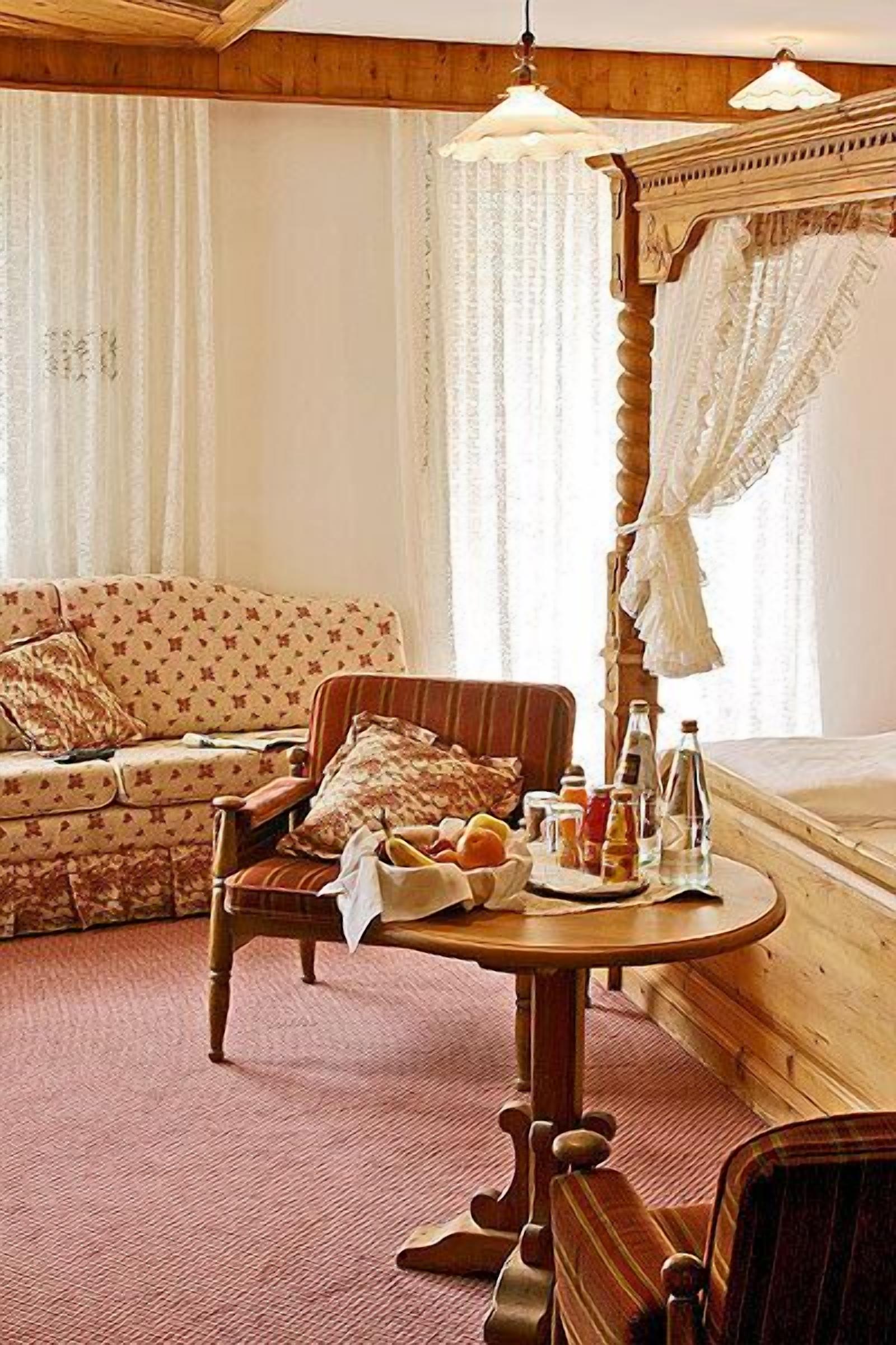 Um quarto acolhedor com cama de madeira, sofá, poltrona e uma pequena mesa com itens de café da manhã.