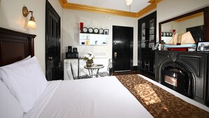 Una habitación de hotel con una cama grande, una chimenea, una mesita con un florero y un reloj de pared.