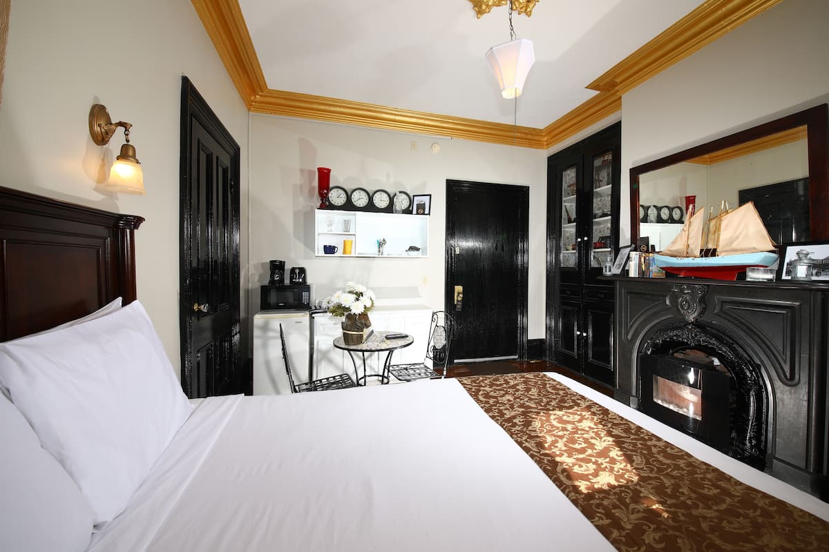 A hotel room with a large bed, a fireplace, a small table with a vase of flowers, and a wall clock.