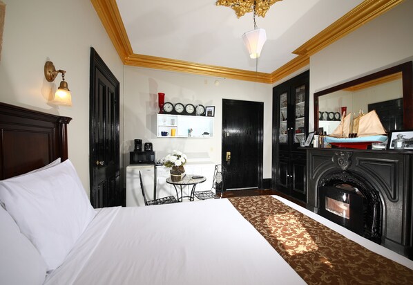 Una habitación de hotel con una cama grande, una chimenea, una mesita con un florero y un reloj de pared.