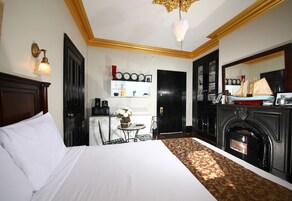A hotel room with a large bed, a fireplace, a small table with a vase of flowers, and a wall clock.